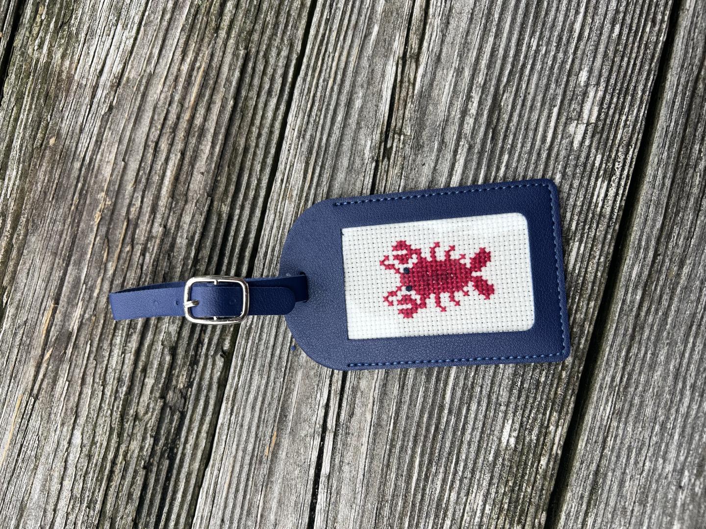 Blue luggage tag with a red scorpion design on wooden background.