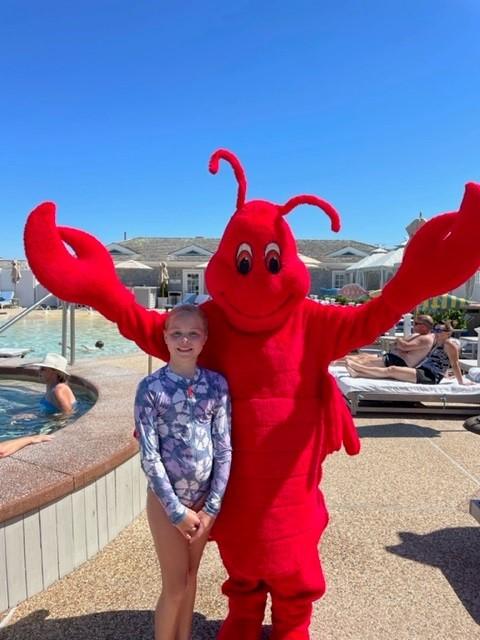 Child posing with a person in a red lobster costume by a pool.