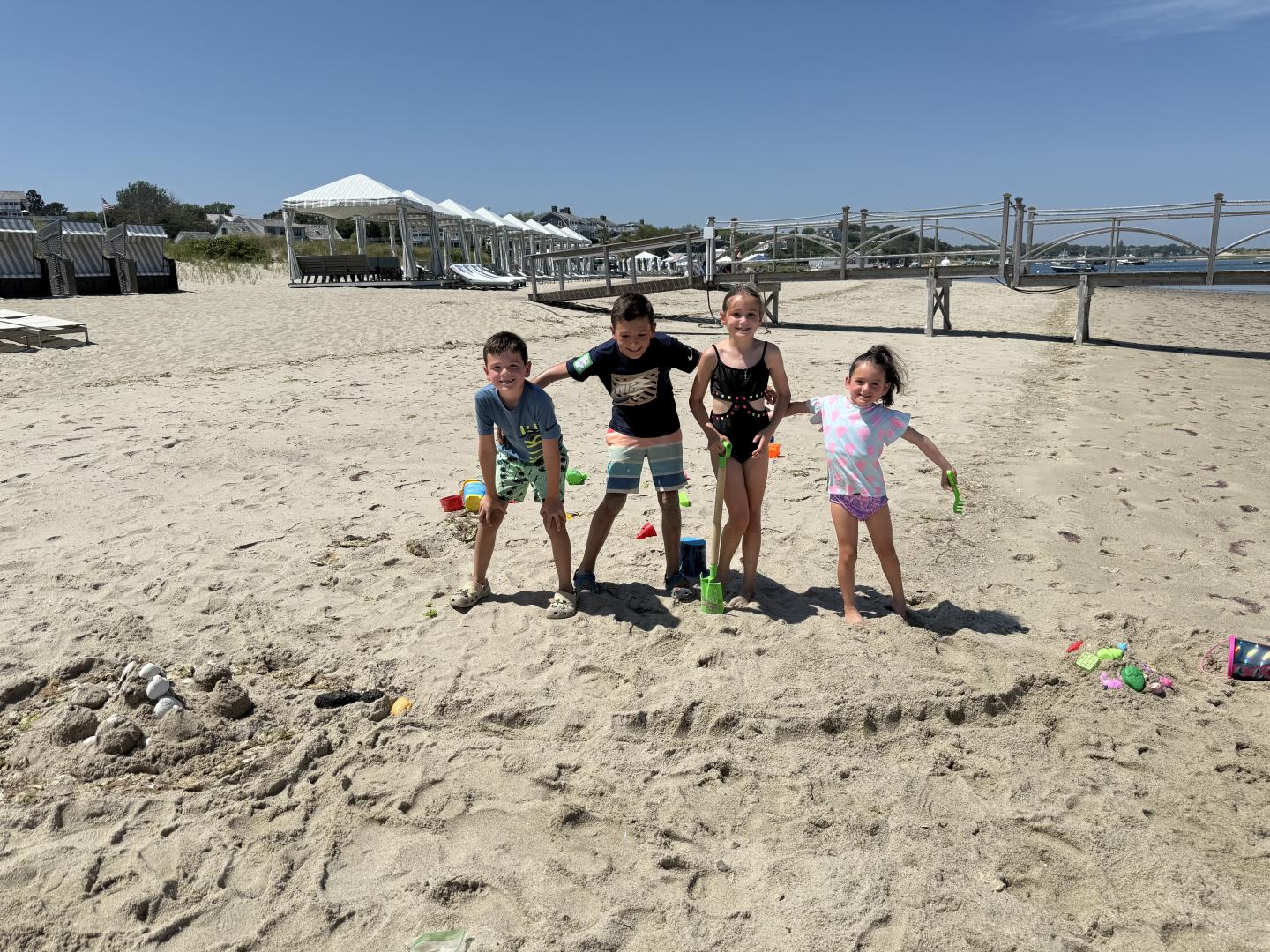 Children playing on a sandy beach with toys, under a clear blue sky.
