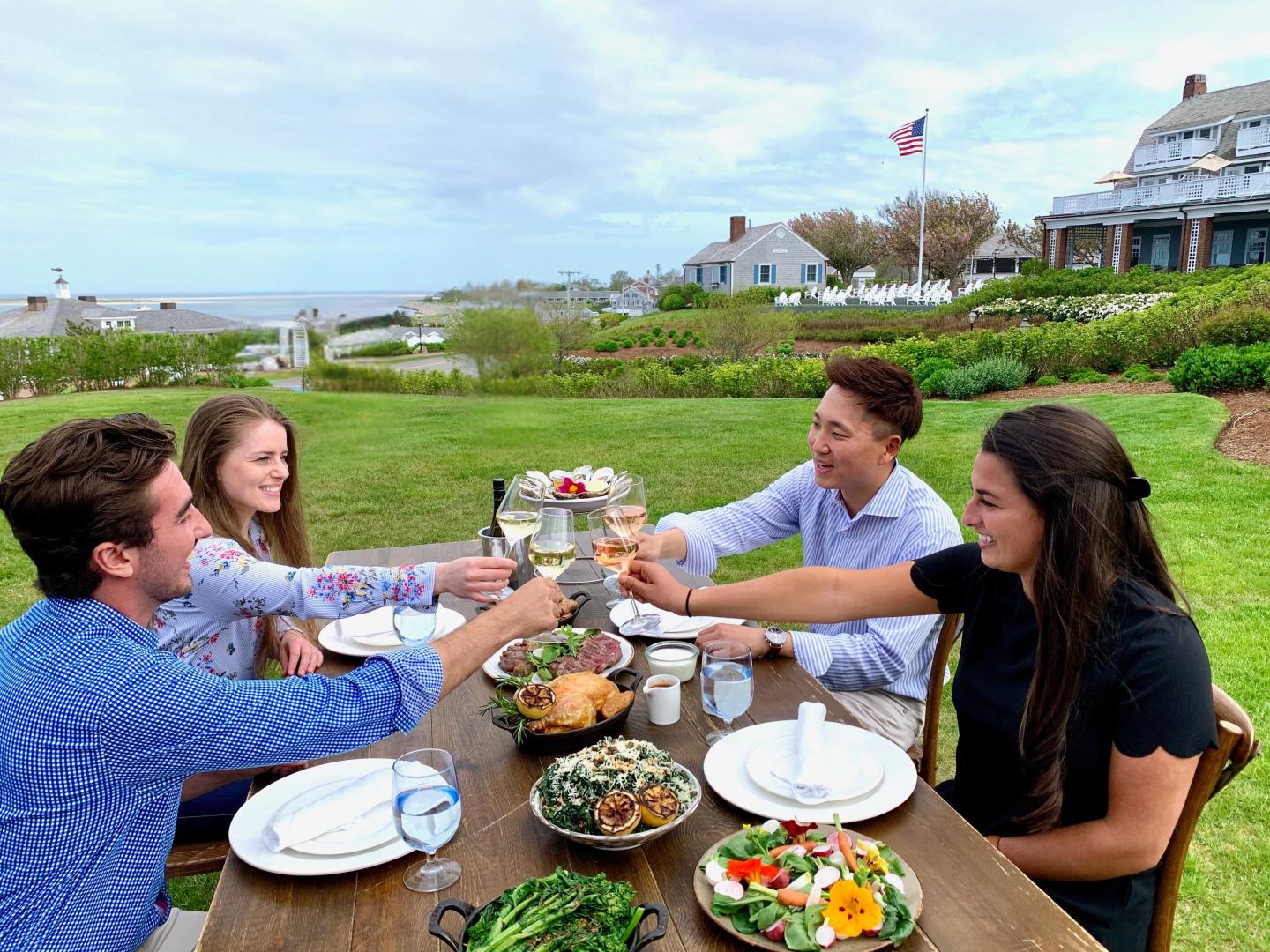 Friends clinking glasses at an outdoor dining table by the sea.
