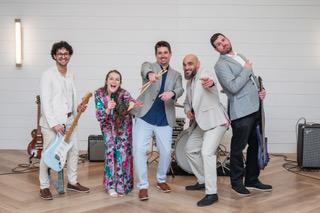 Band members posing with instruments, smiling in a bright room.