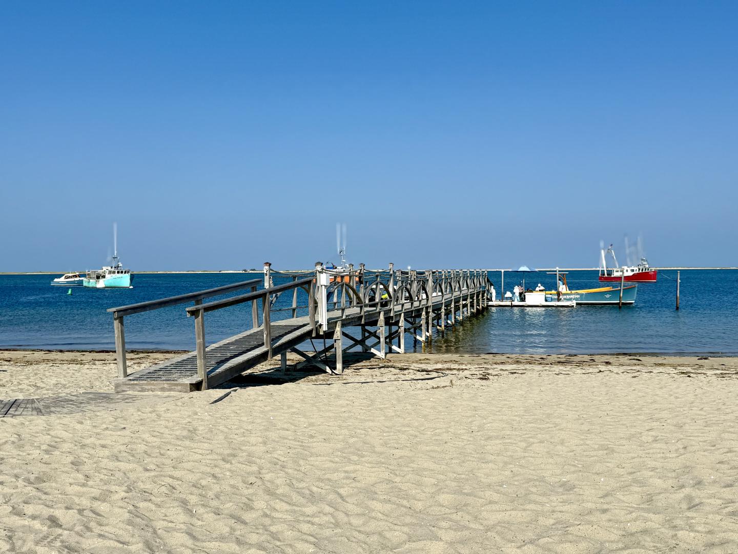 Wooden pier extends into calm blue sea, boats in the distance.