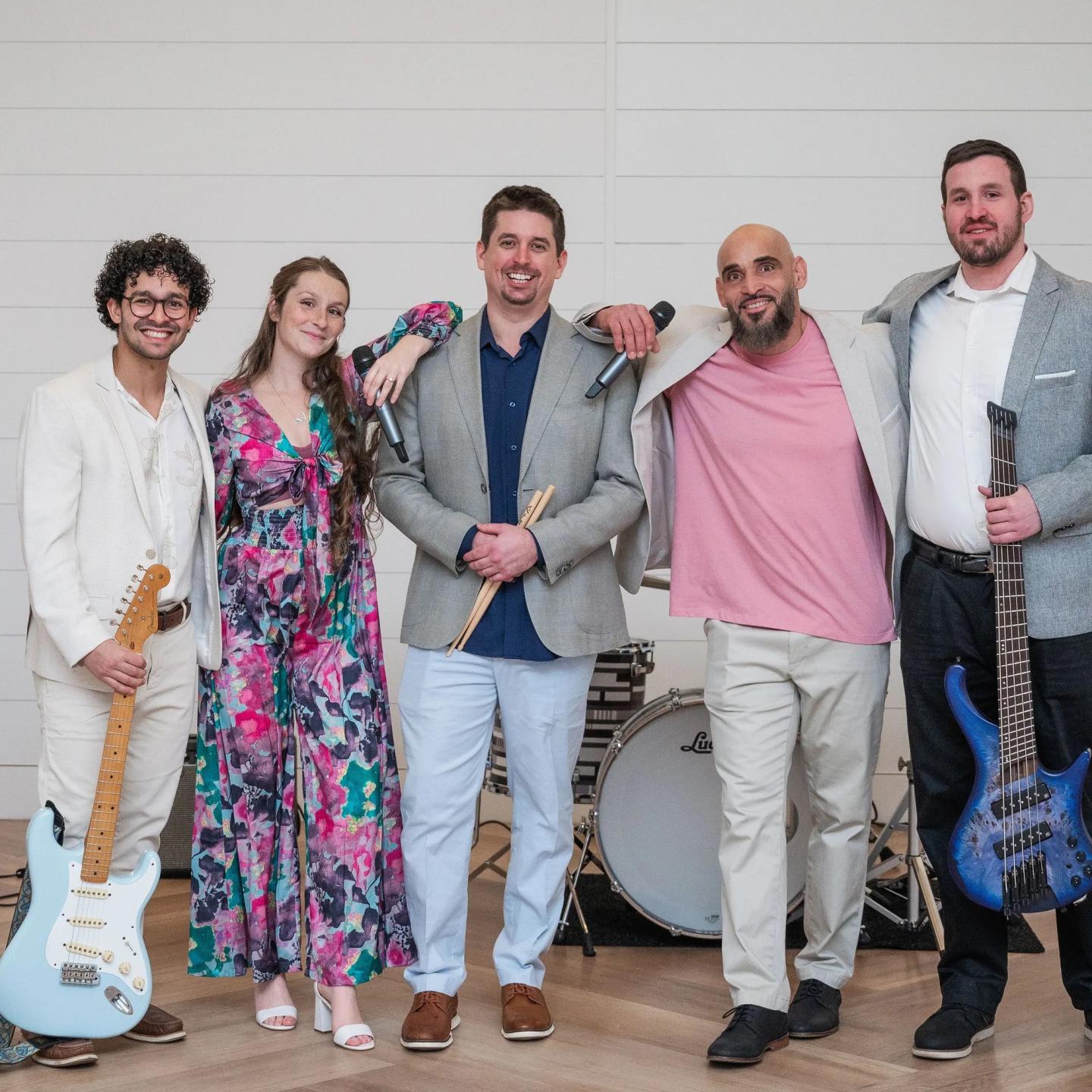 Band members pose with instruments in front of a drum set, wearing colorful outfits.