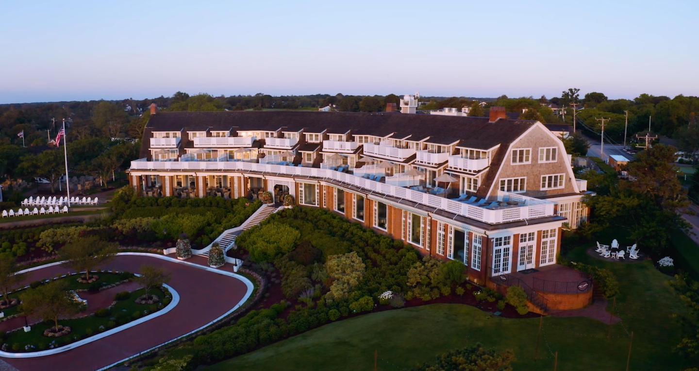 Large hotel with balconies, surrounded by lush greenery at sunset.