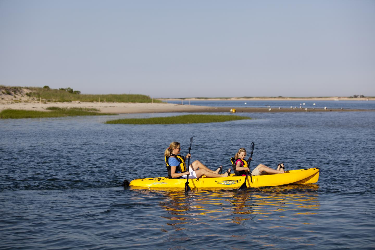 Two people kayaking in a yellow kayak on a calm lake under a clear blue sky.