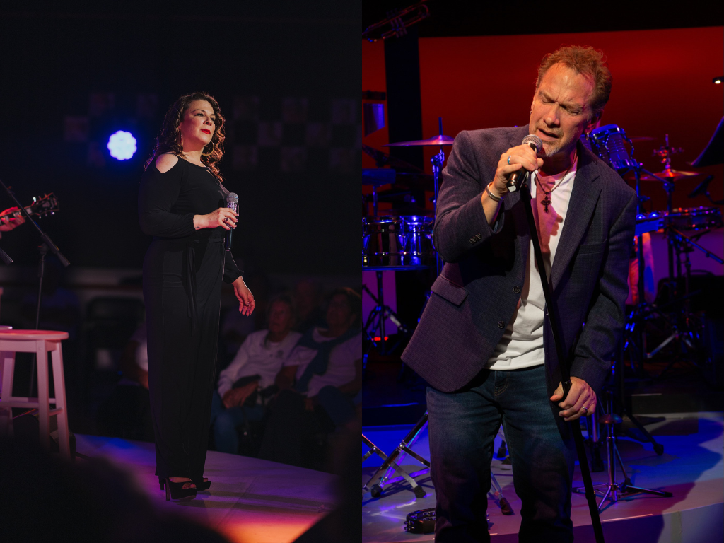 Two singers on stage, one in black, one in a blazer, both holding microphones.
