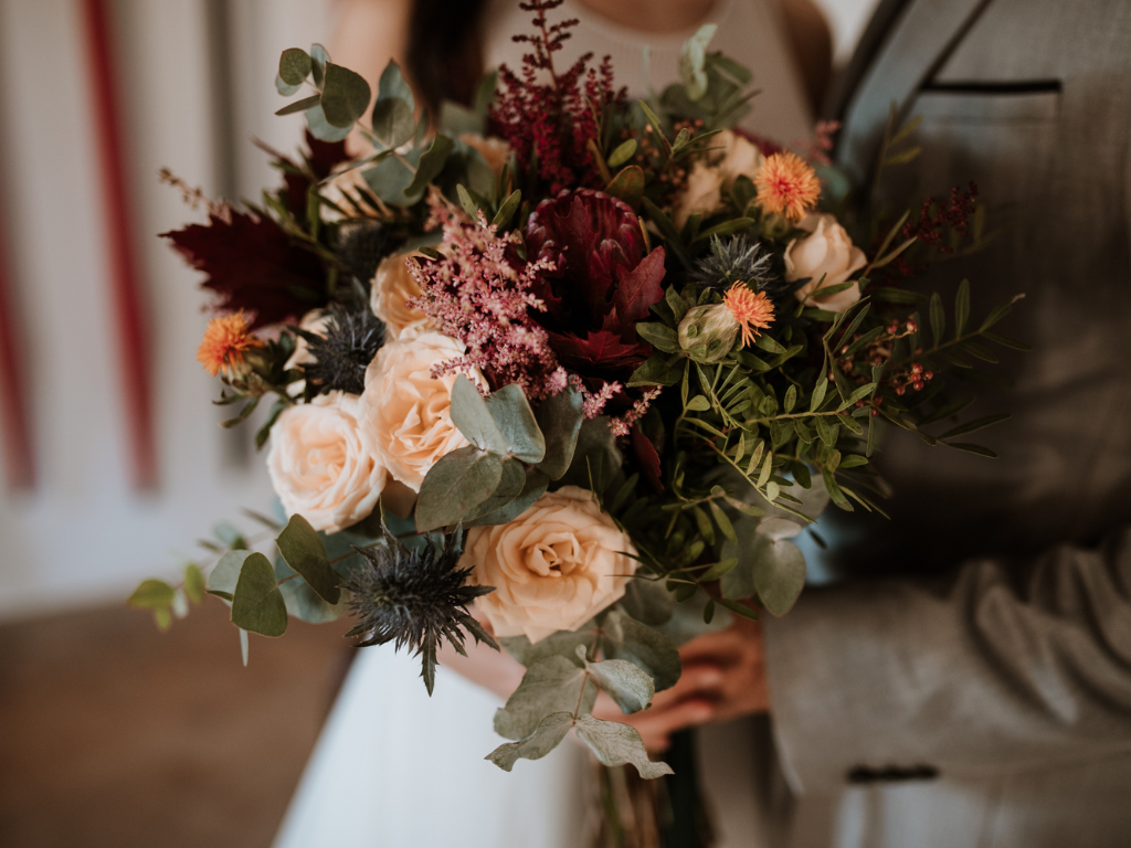 Bridal bouquet with roses and greenery held by couple in formal attire.