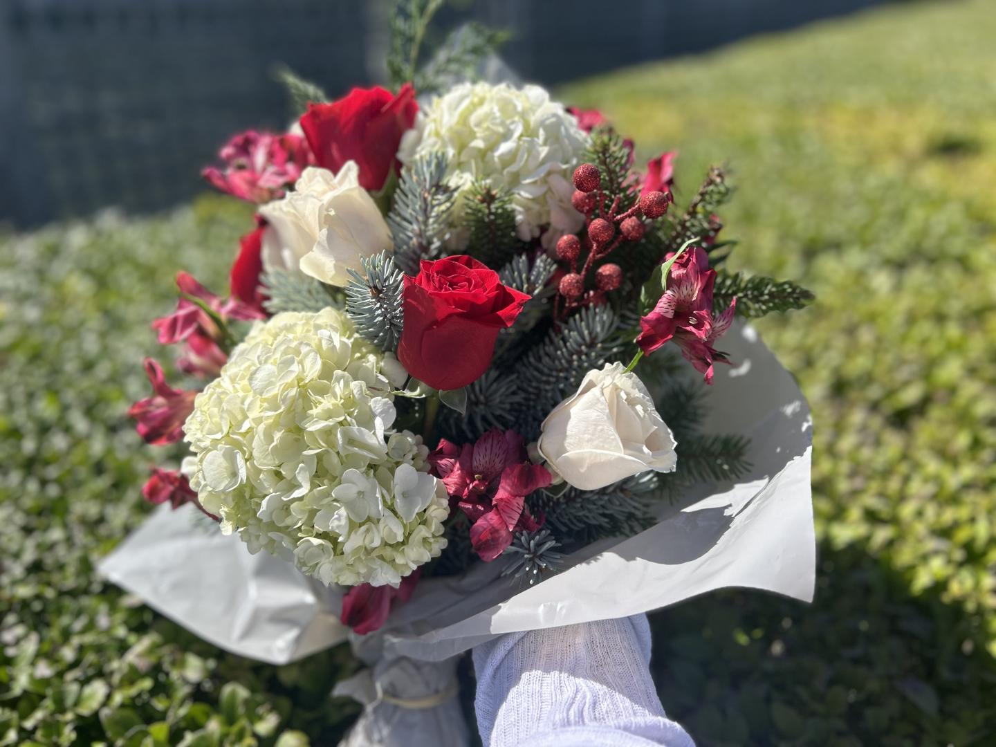 Bouquet with red roses, white hydrangeas, and greenery on a sunny lawn.