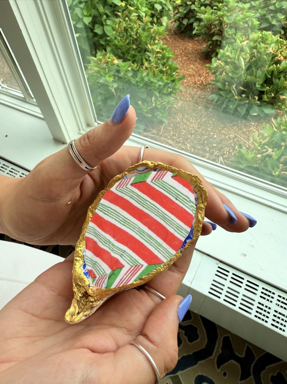 Gold leaf-shaped object with red and green stripes, held by hands near a window.