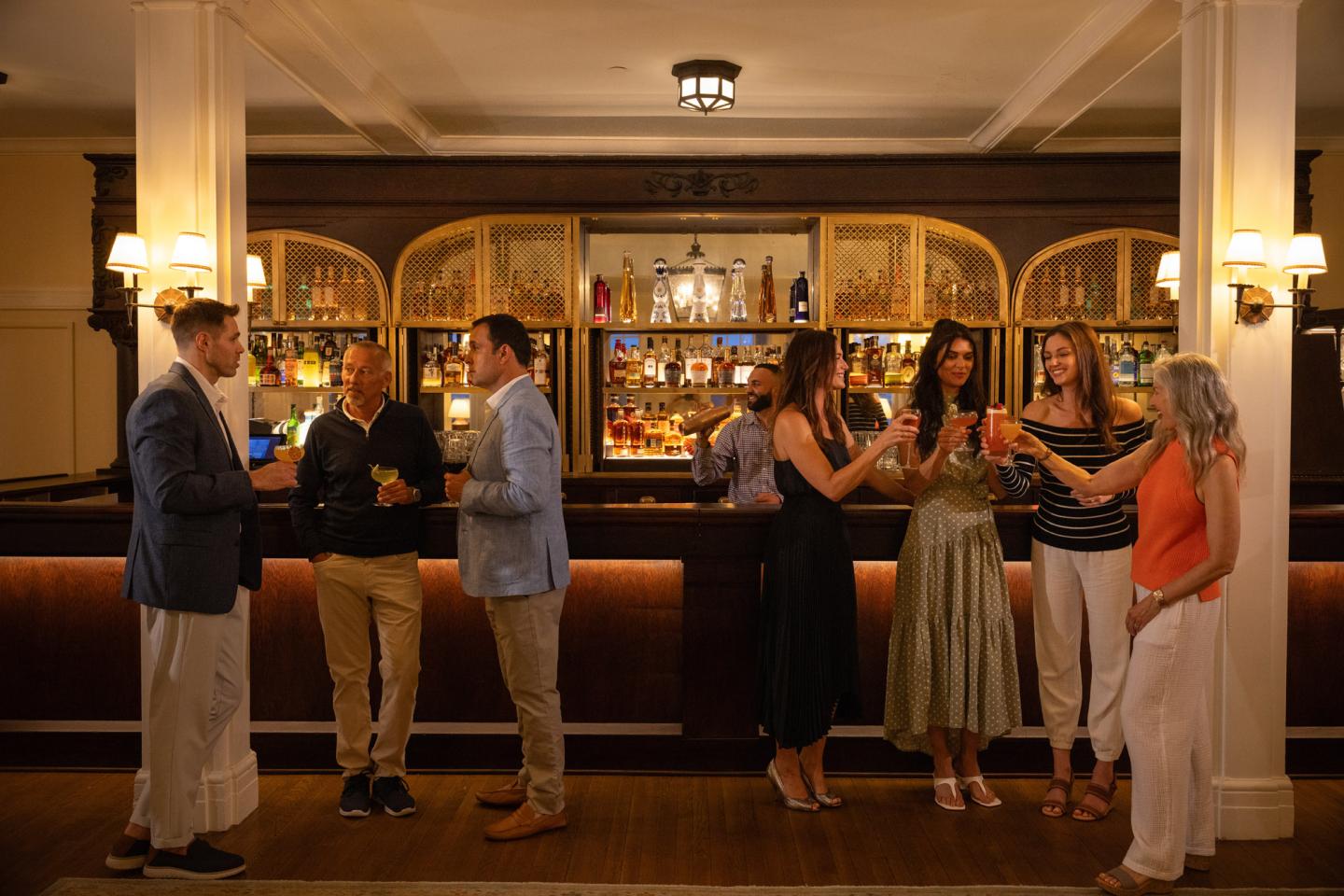 People socializing at a bar, bartender serving drinks, warm lighting.