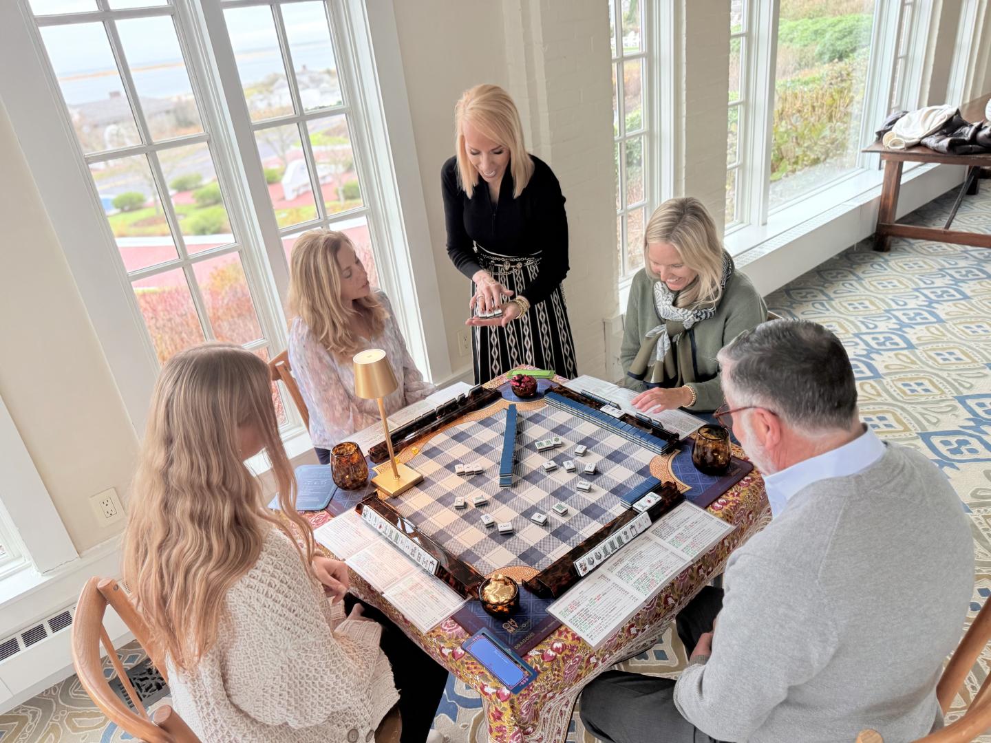 Four people playing a board game in a bright room with large windows.