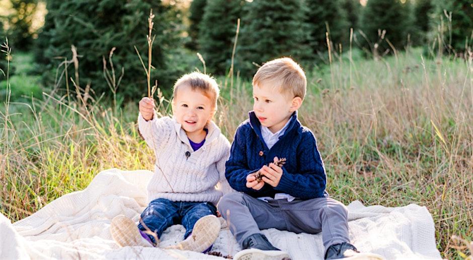 Two young children sitting on a blanket in a sunny field.