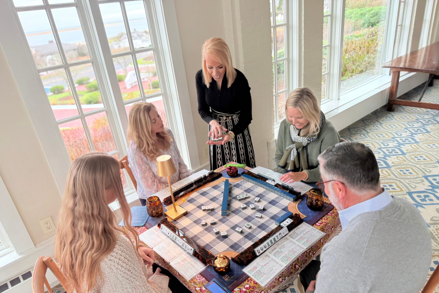 Group playing a board game in a bright room with large windows.