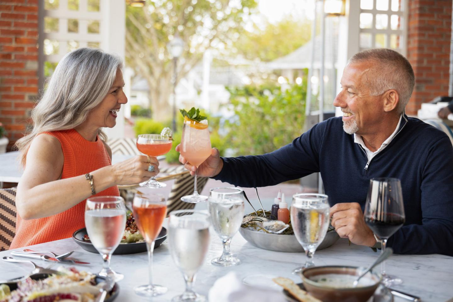 Older couple toasting at an outdoor restaurant table, smiling.