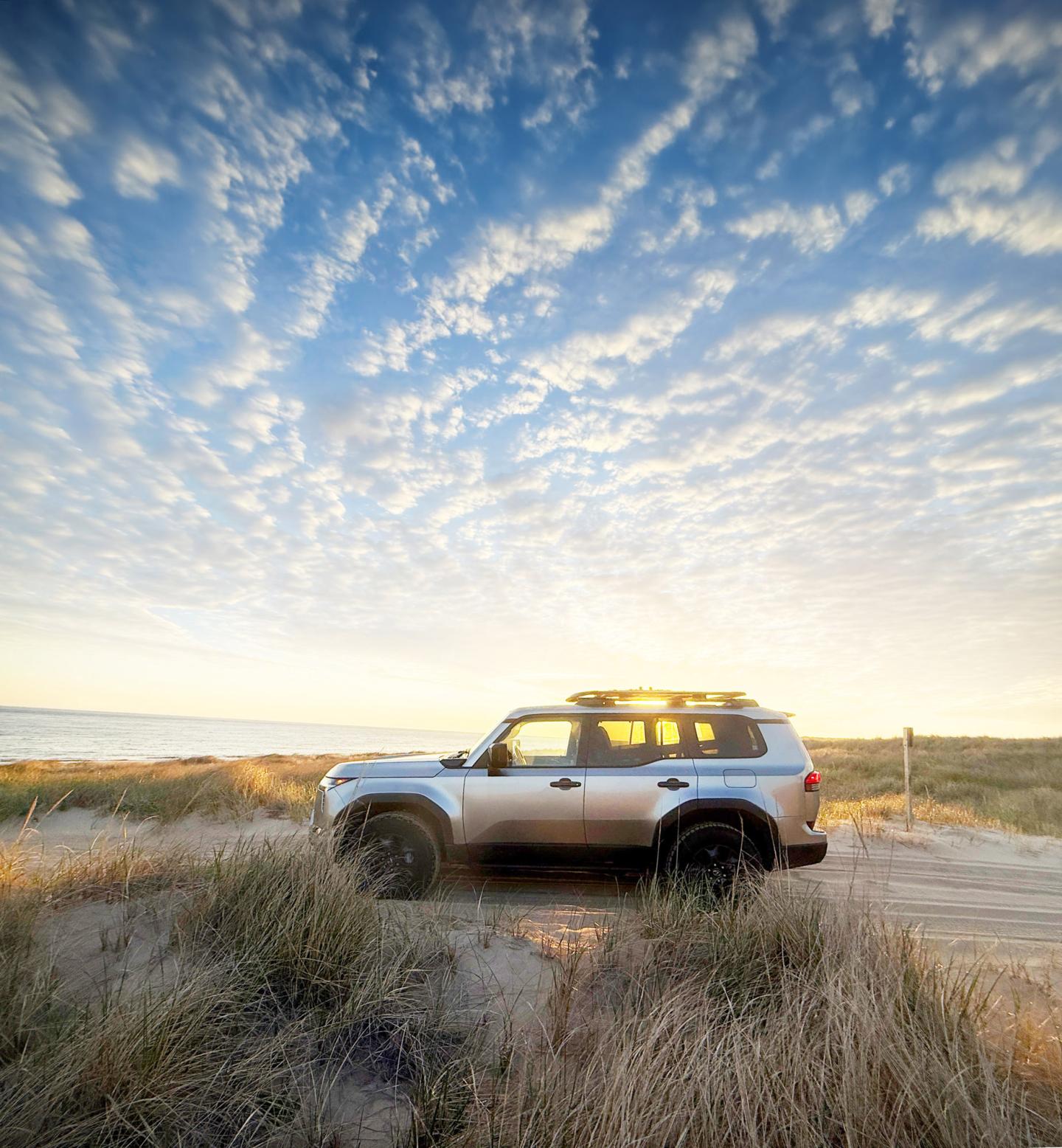 SUV on a sandy beach path under a dramatic, cloud-filled sky.