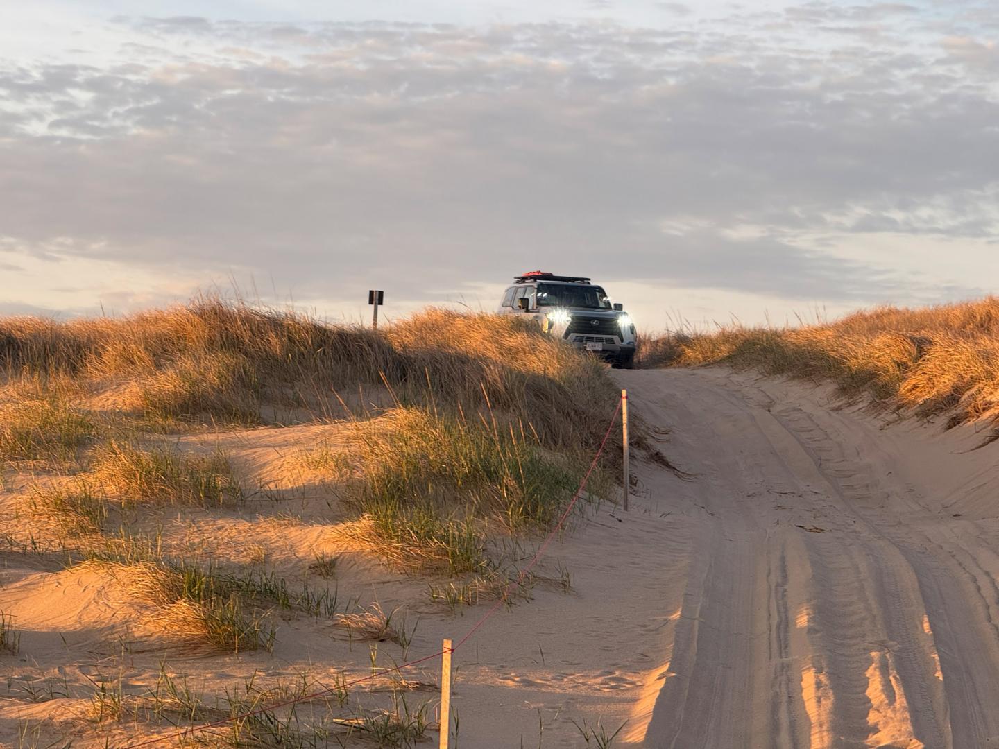 SUV driving on sandy dunes at sunset.