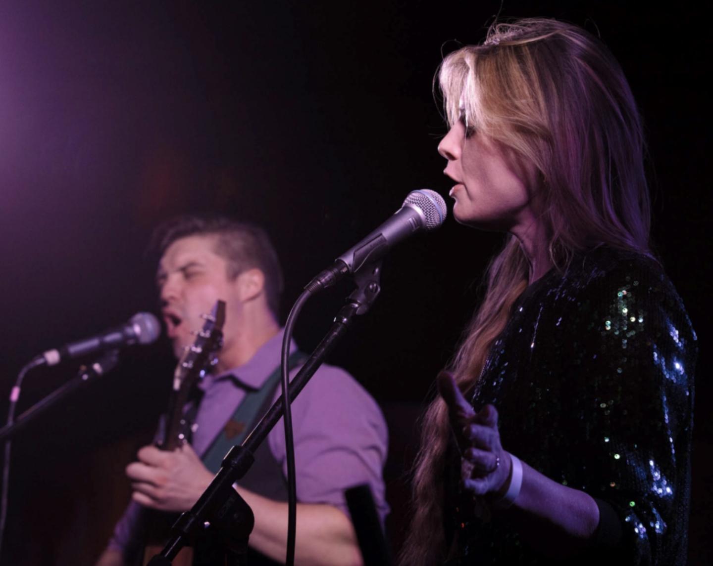 Two musicians performing on stage, singing into microphones.