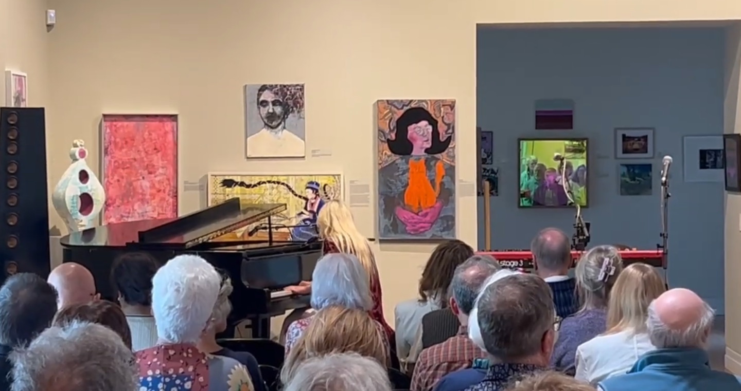 Concert with pianist and audience in an art gallery. Bright artwork on walls.