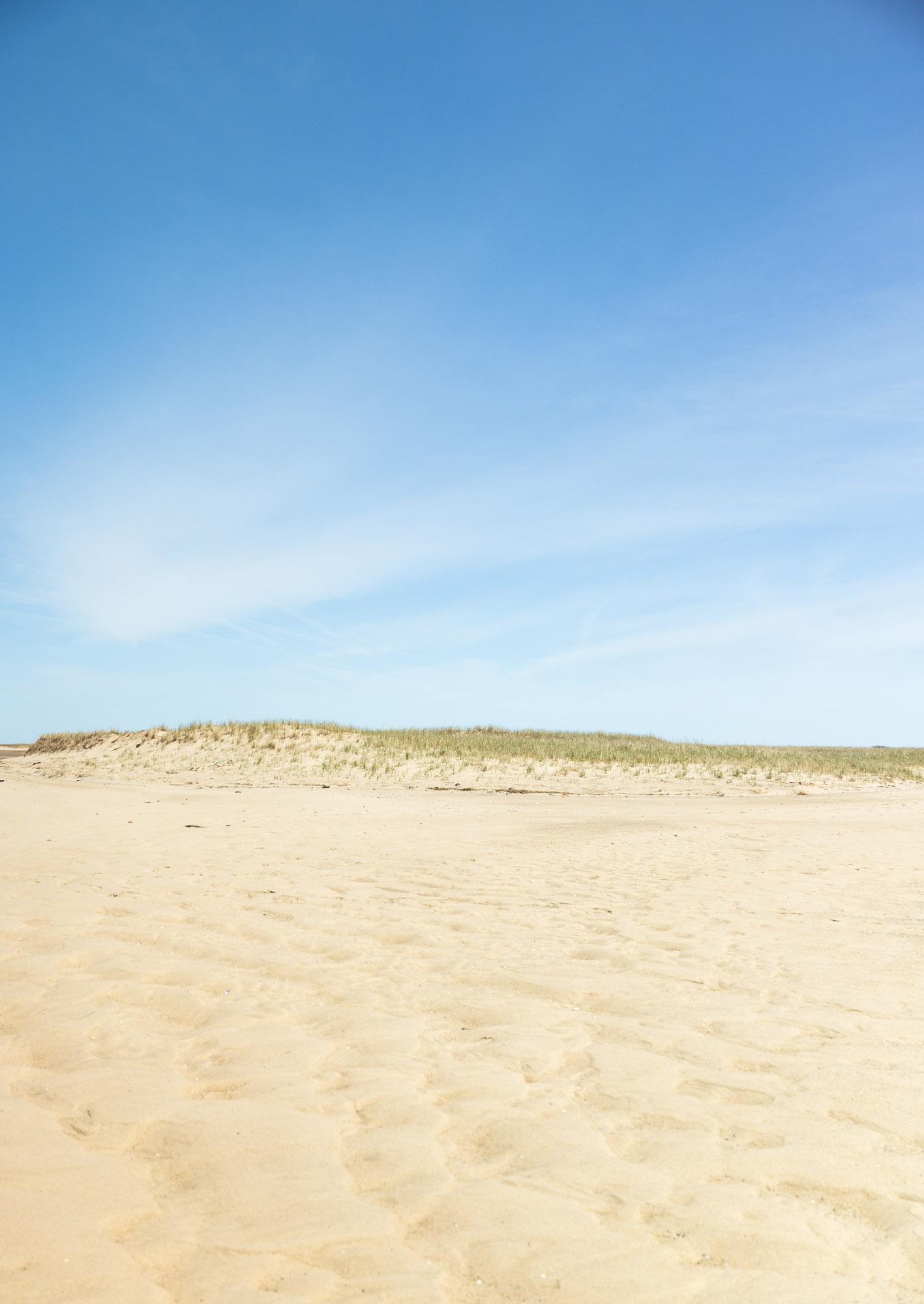 Sunny beach with sand dunes under a bright blue sky.
