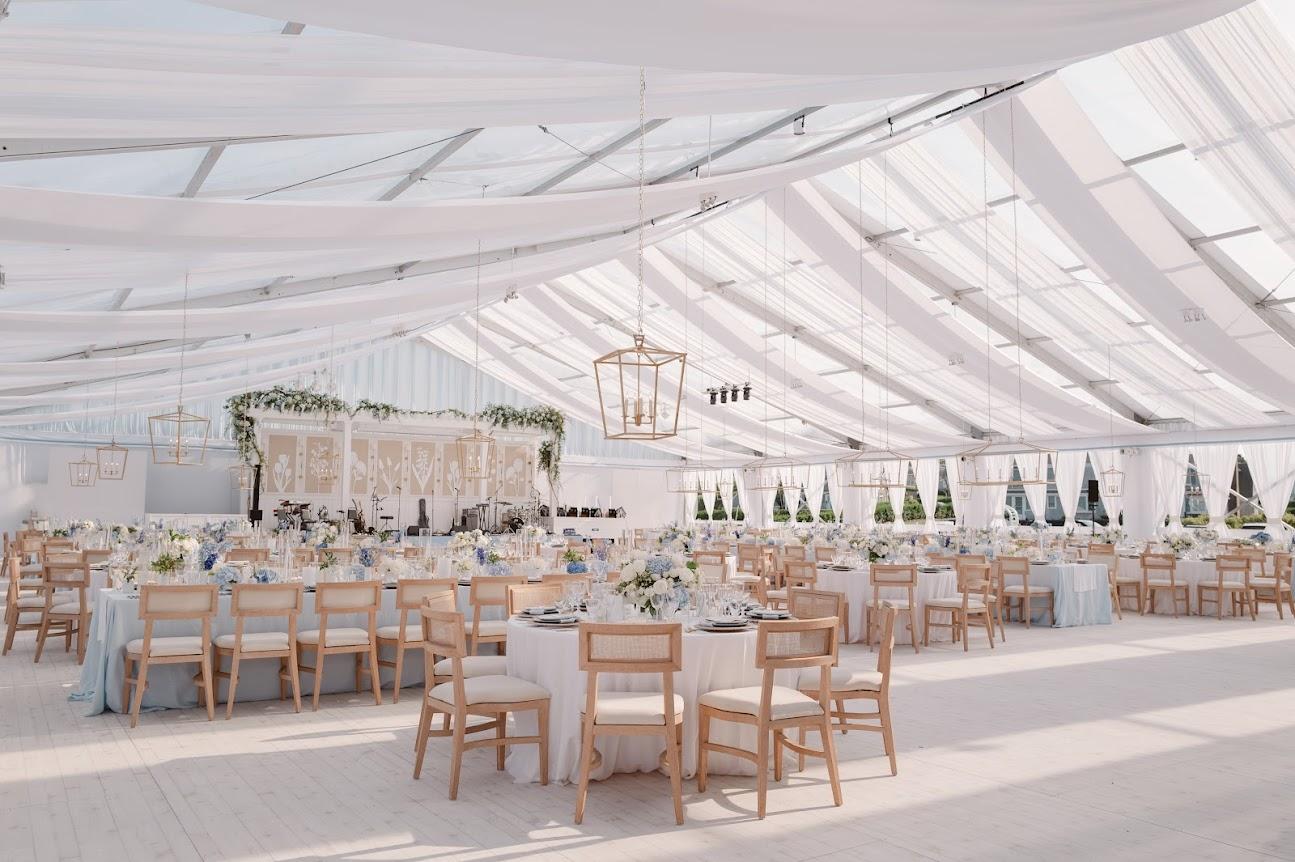 Elegant wedding reception in a spacious, white tent with round tables and chairs.