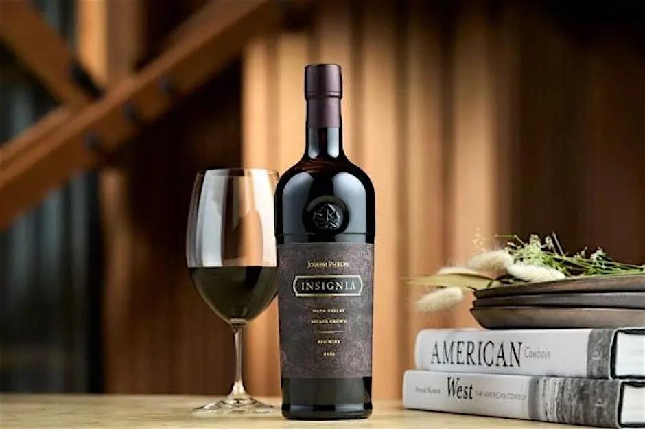 Wine bottle and glass on table with books and plant, wooden background.