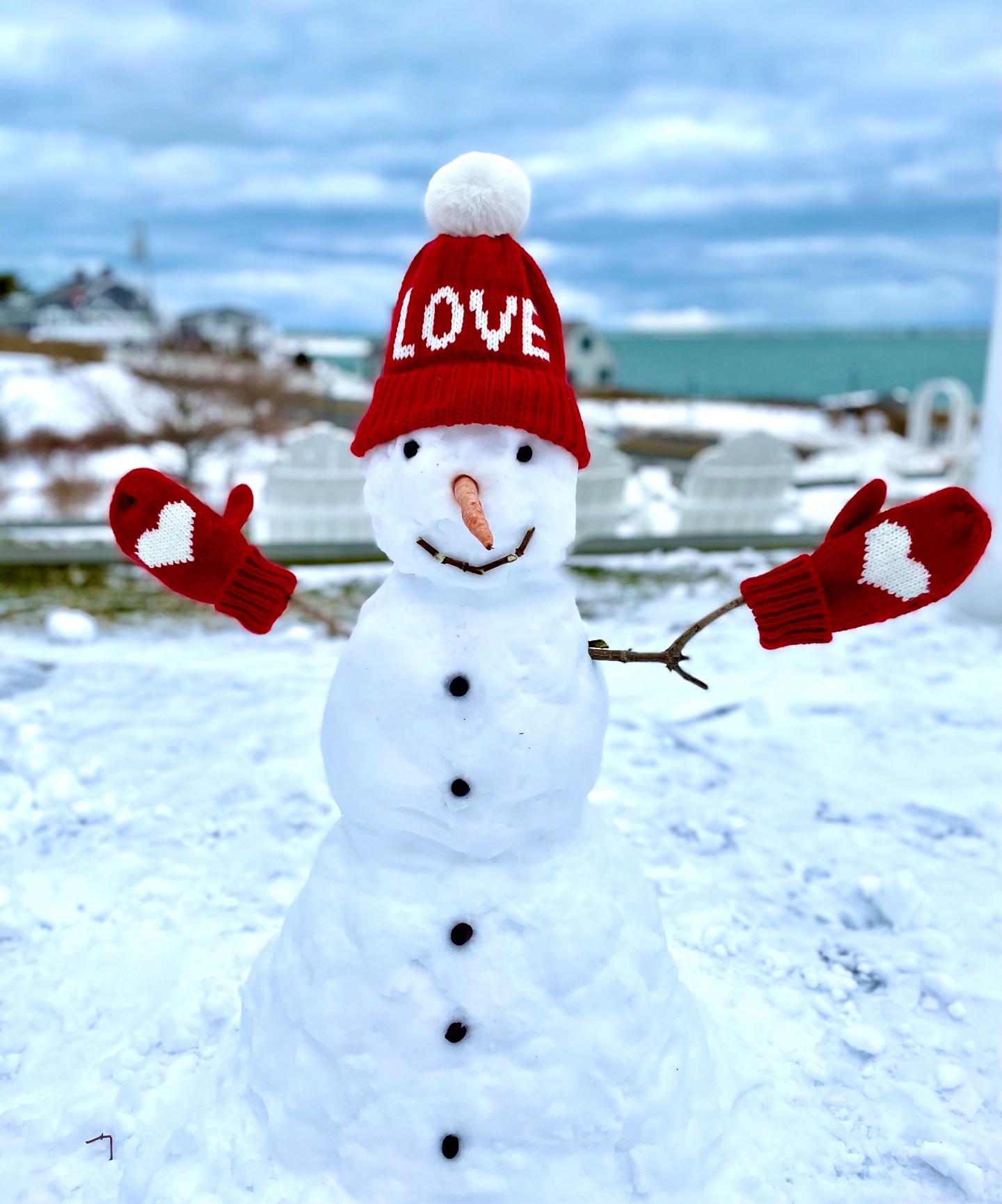 Snowman with red hat and mittens, smiling on a snowy landscape.
