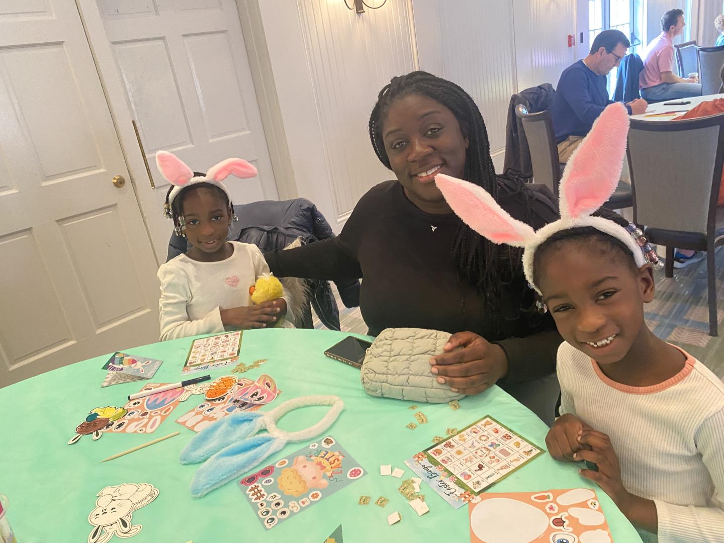 Family at a table, children wearing bunny ears, crafting and playing games.