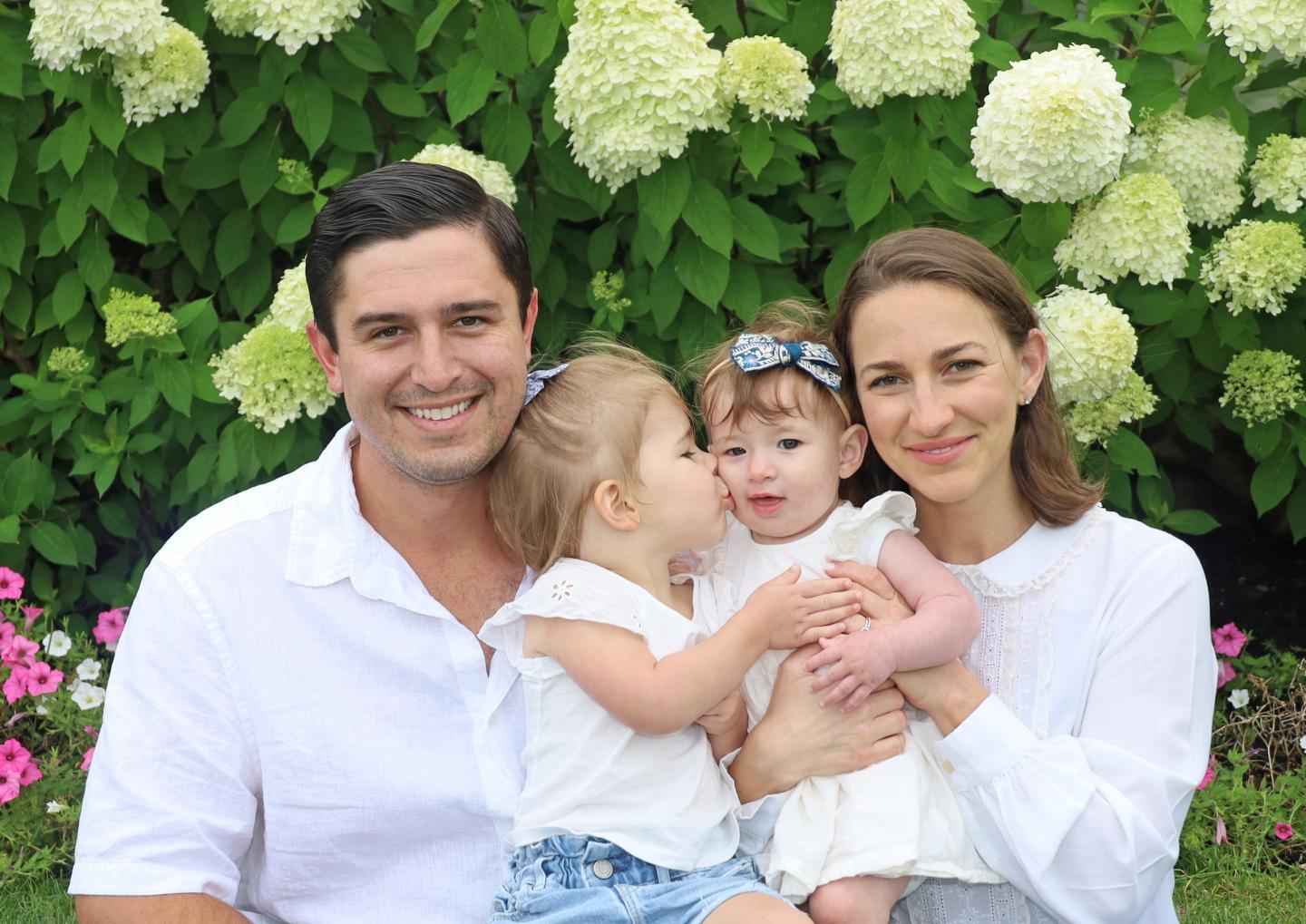 Family of four smiling, sitting in a garden with hydrangeas.