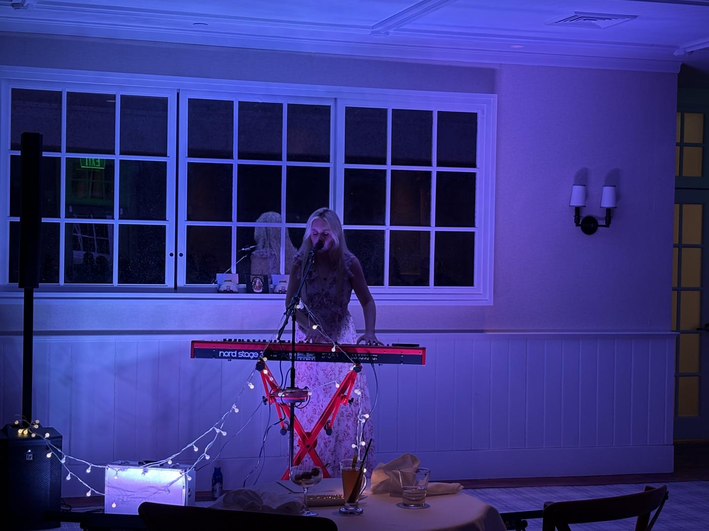 Musician playing keyboard under blue lighting in a cozy room with fairy lights.
