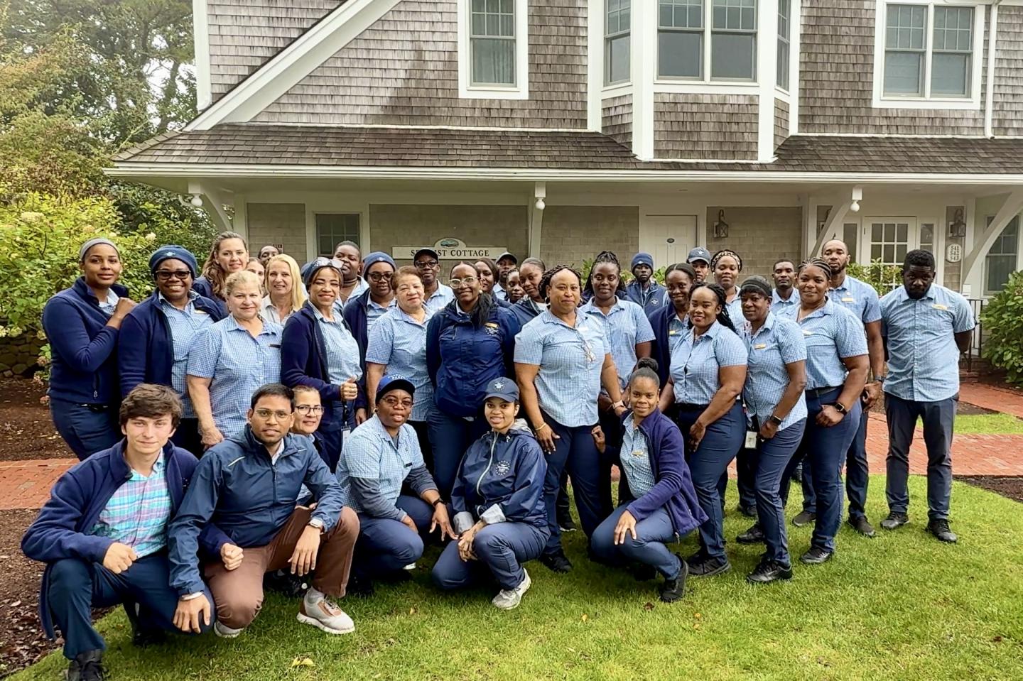 Large group in blue uniforms poses in front of a house.
