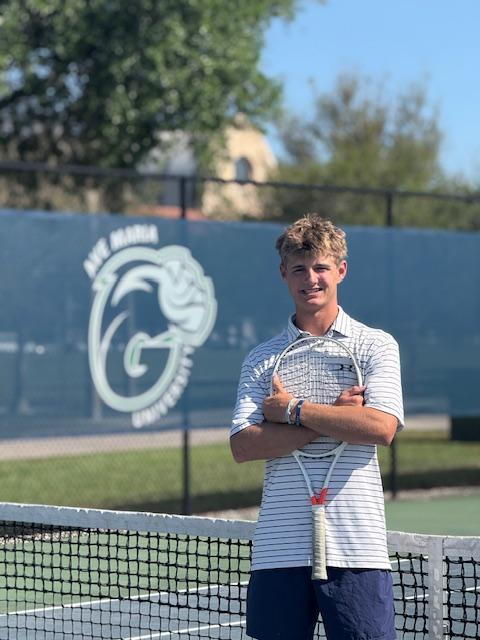 Man holding a tennis racket on a sunny tennis court, with a logo in the background.