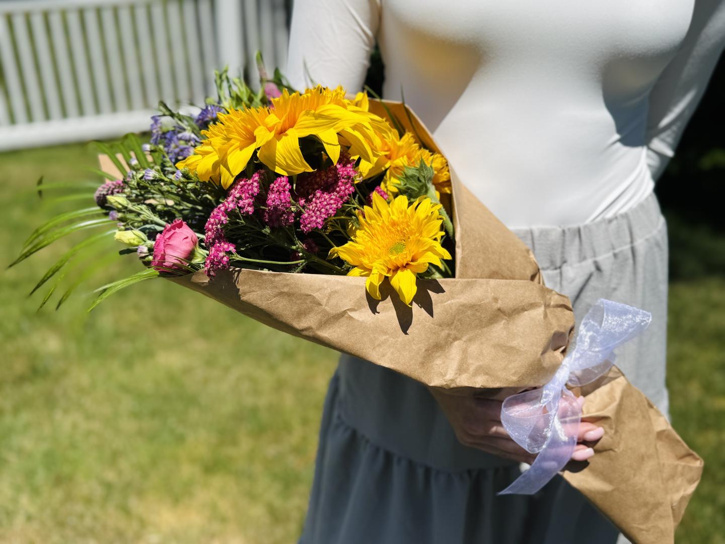 A person holds a bouquet of sunflowers and purple flowers outdoors.
