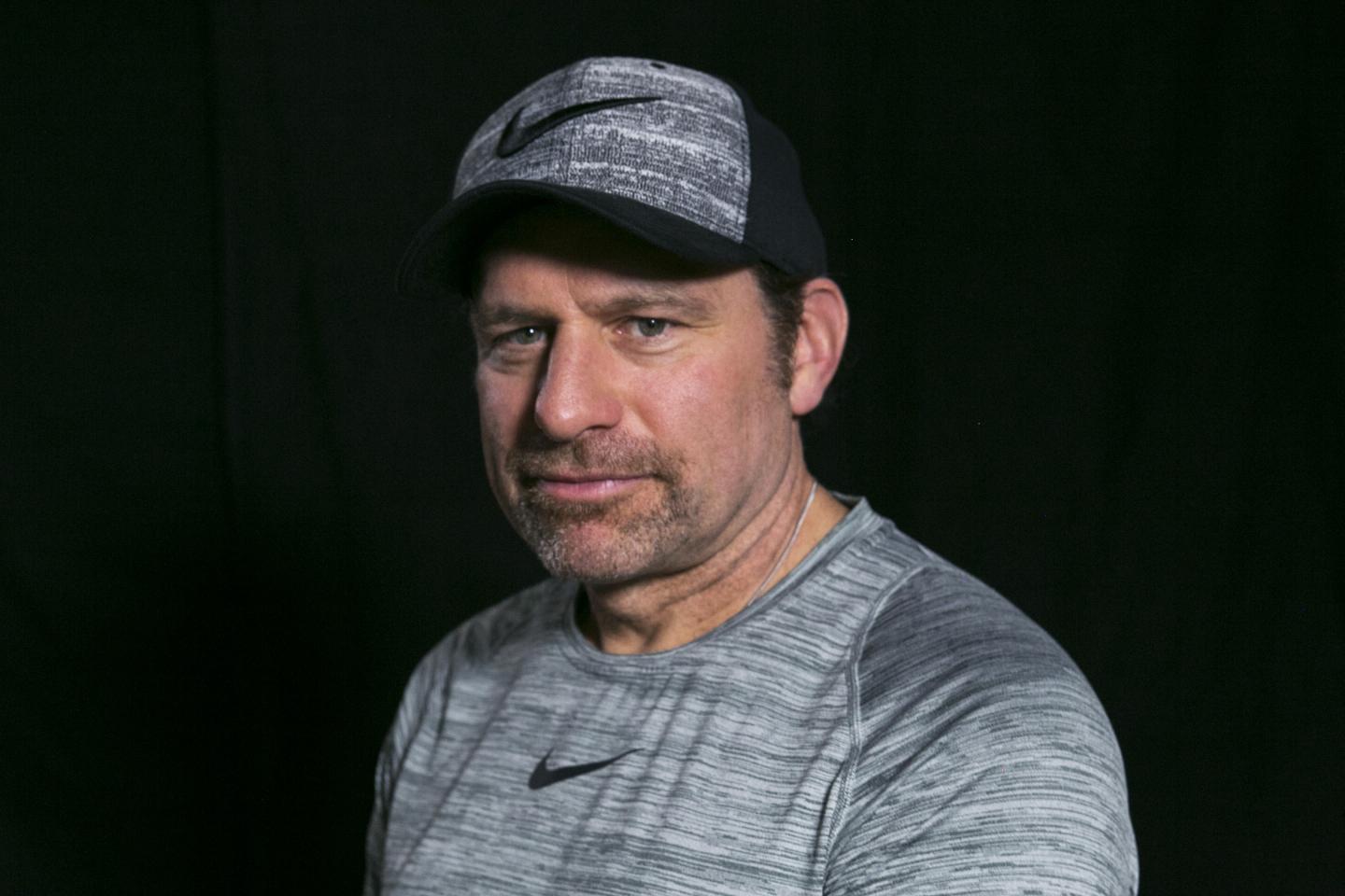 Man in a gray shirt and cap, against a dark background.