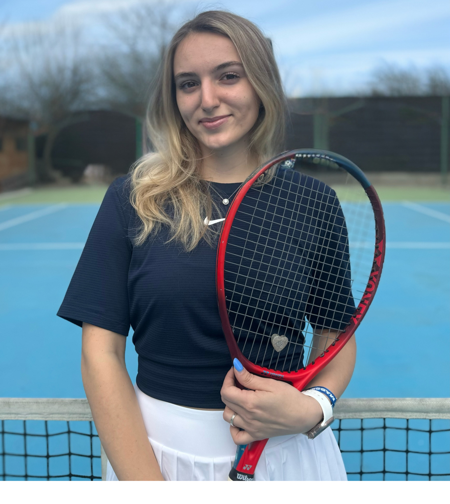 Woman holding tennis racket on outdoor court, smiling.