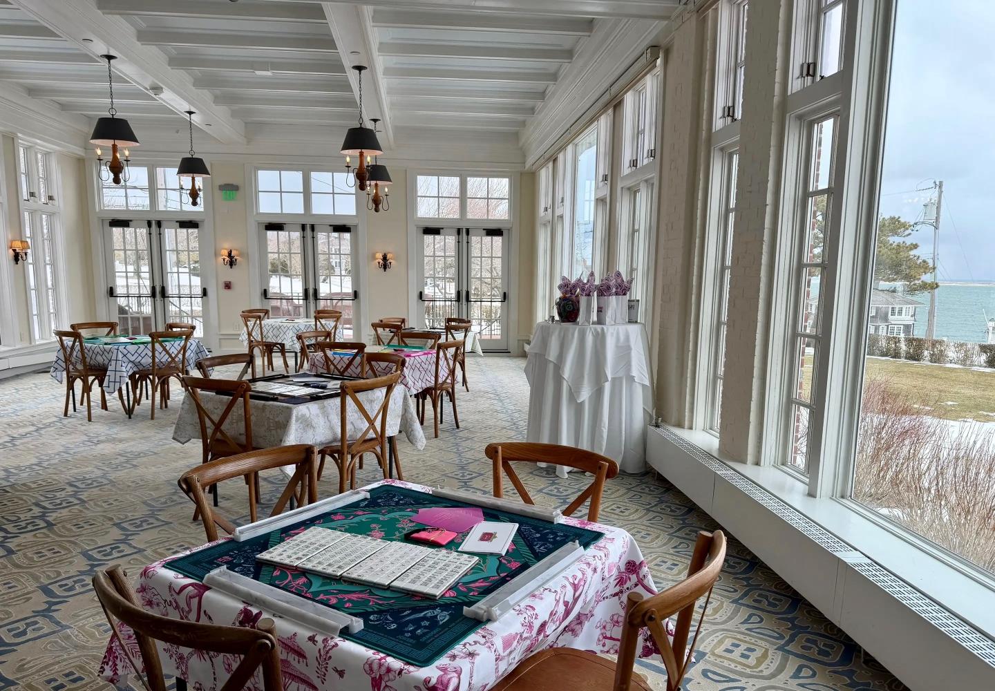 Bright dining area with wooden chairs, set tables, and large windows facing outside.