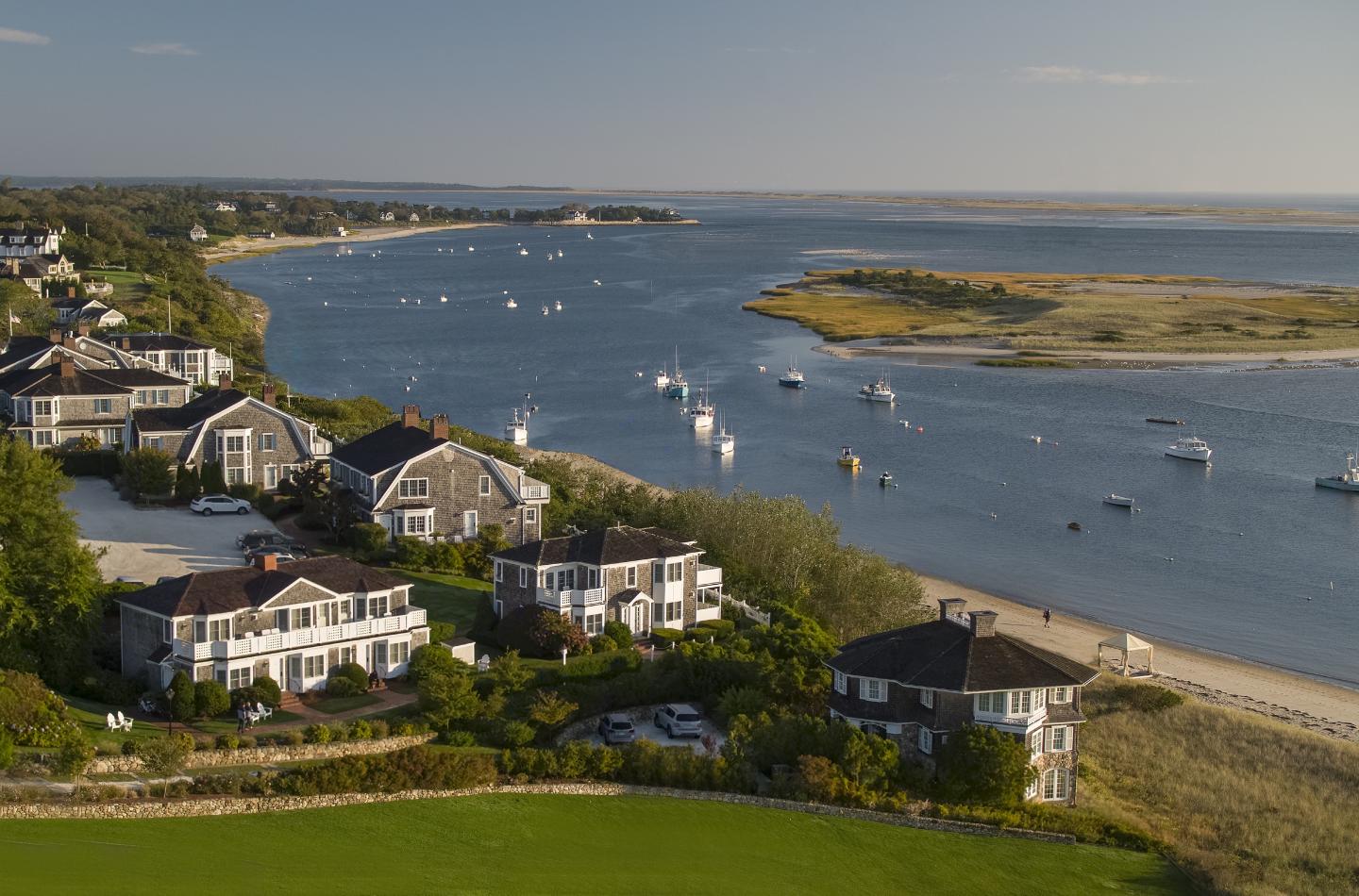 Coastal houses by a river with boats, under a clear blue sky.