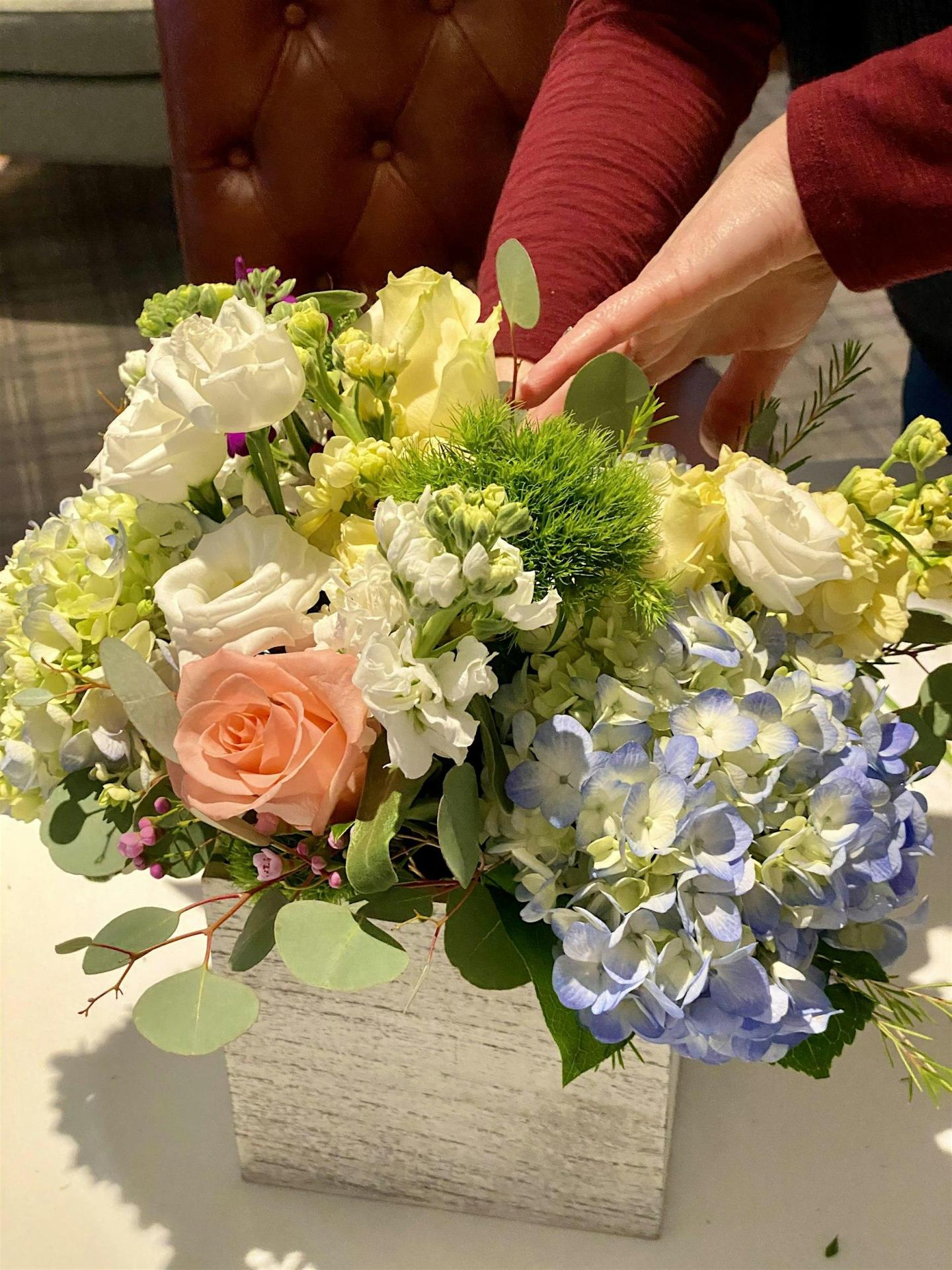 Floral arrangement with roses and blue hydrangeas in a vase, hand adjusting flowers.