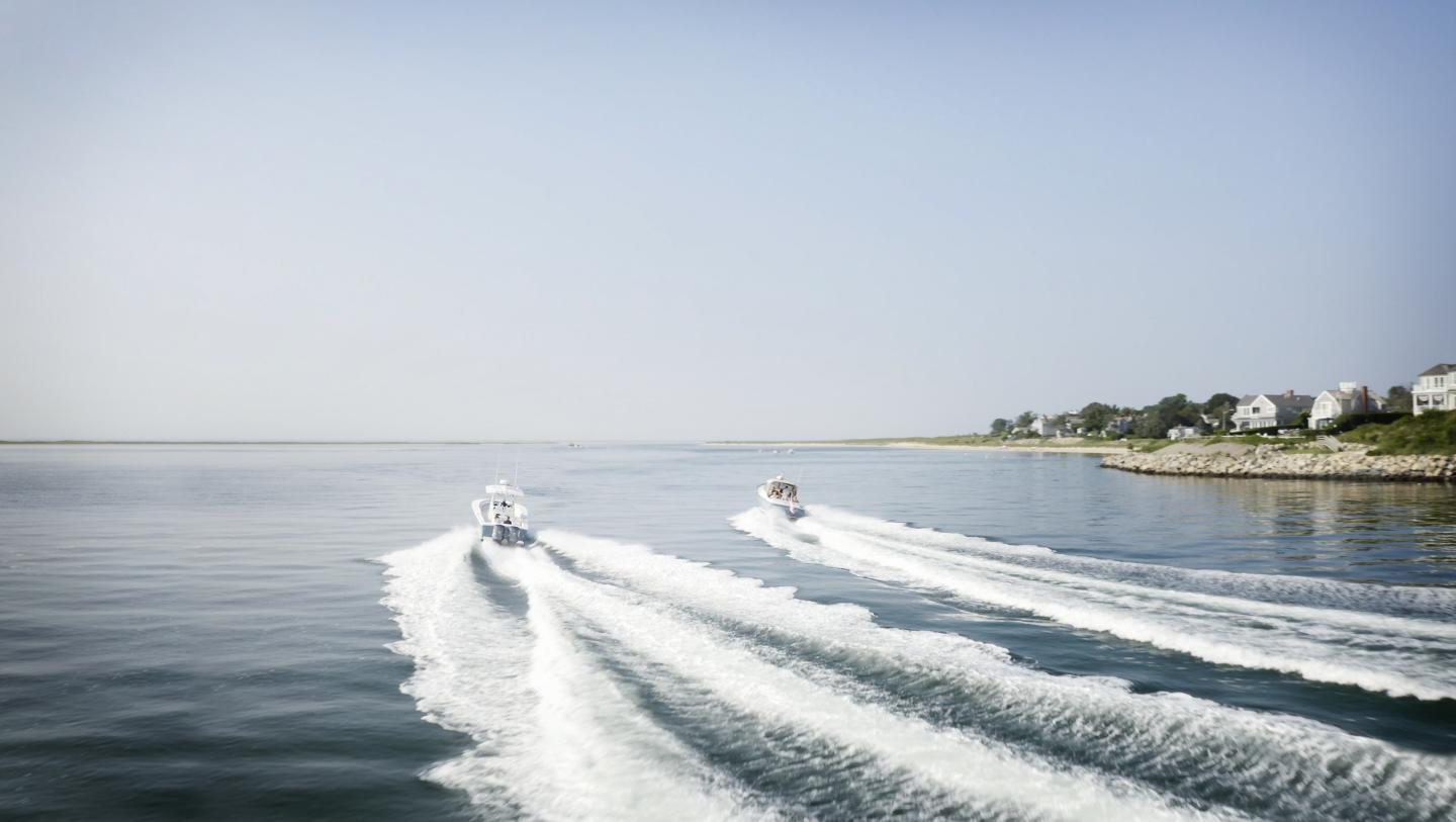 Speedboats creating waves on calm water near a rocky coastline.