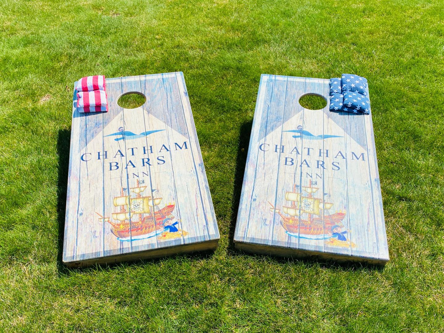 Cornhole boards on grass with bean bags, featuring nautical design.