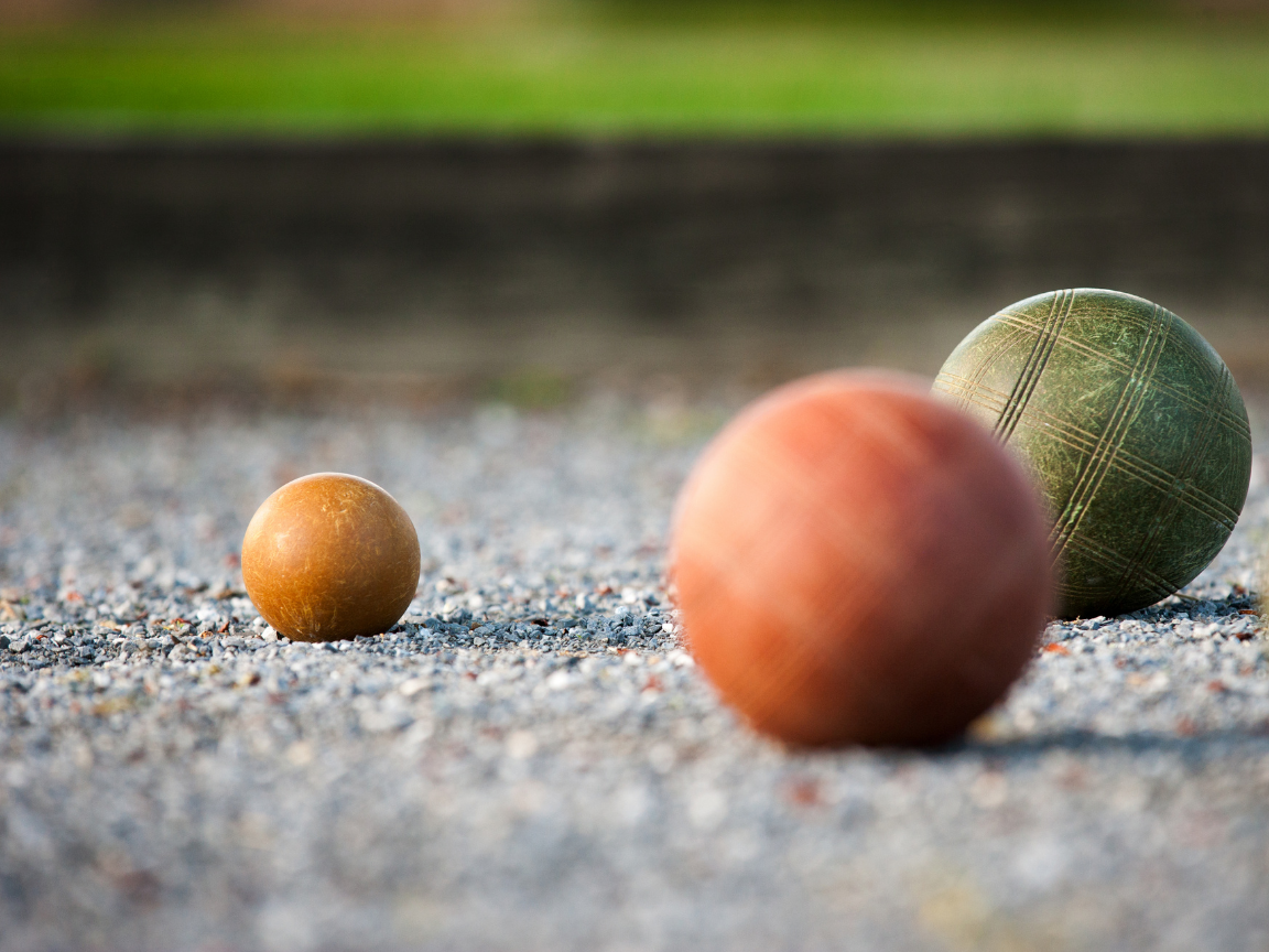 Three bocce balls on gravel, varying sizes and colors, grassy background.